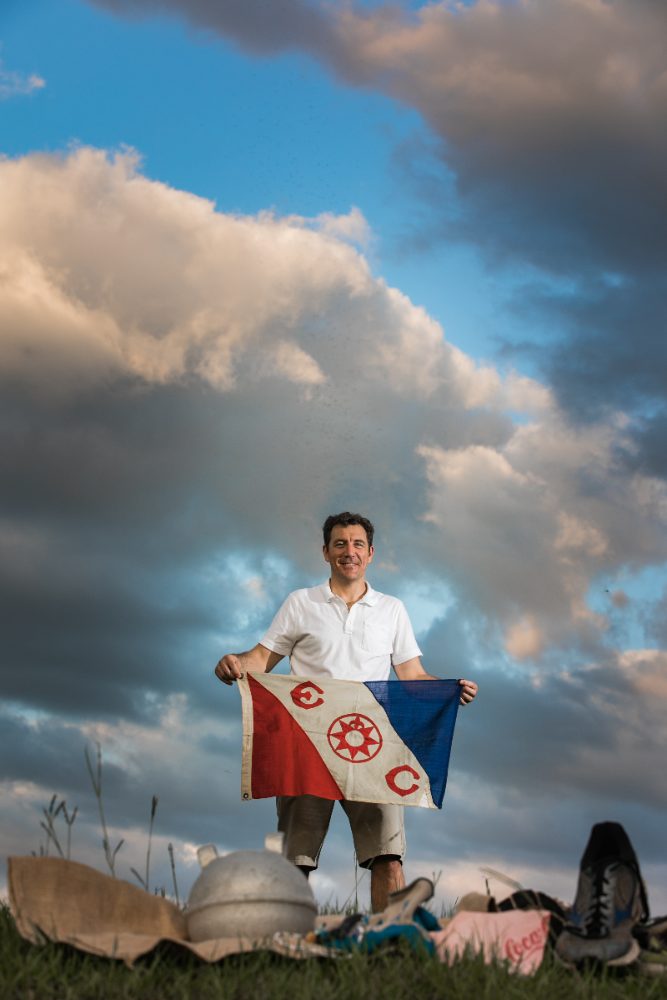 Brett holding an Explorers Club flag under a cloudy sky